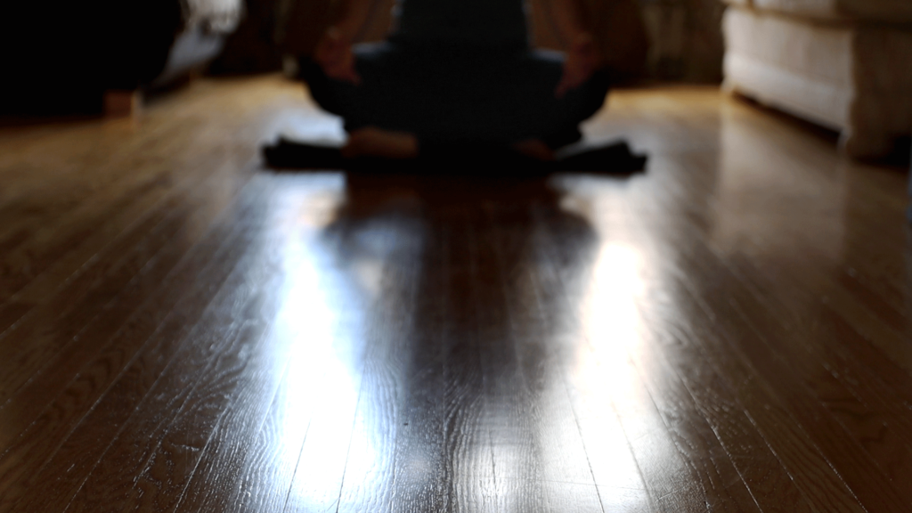 John Francisco sitting in daily meditation practice on a cushion casting a shadow over the illuminated hardwood floor