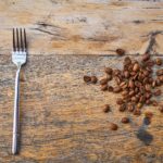 Overhead view of fork next to coffee beans on empty table